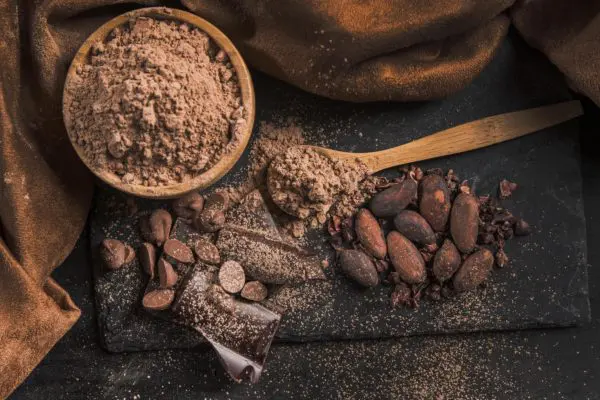 Cacao Powder in a bowl and powder and pods on a wooden table